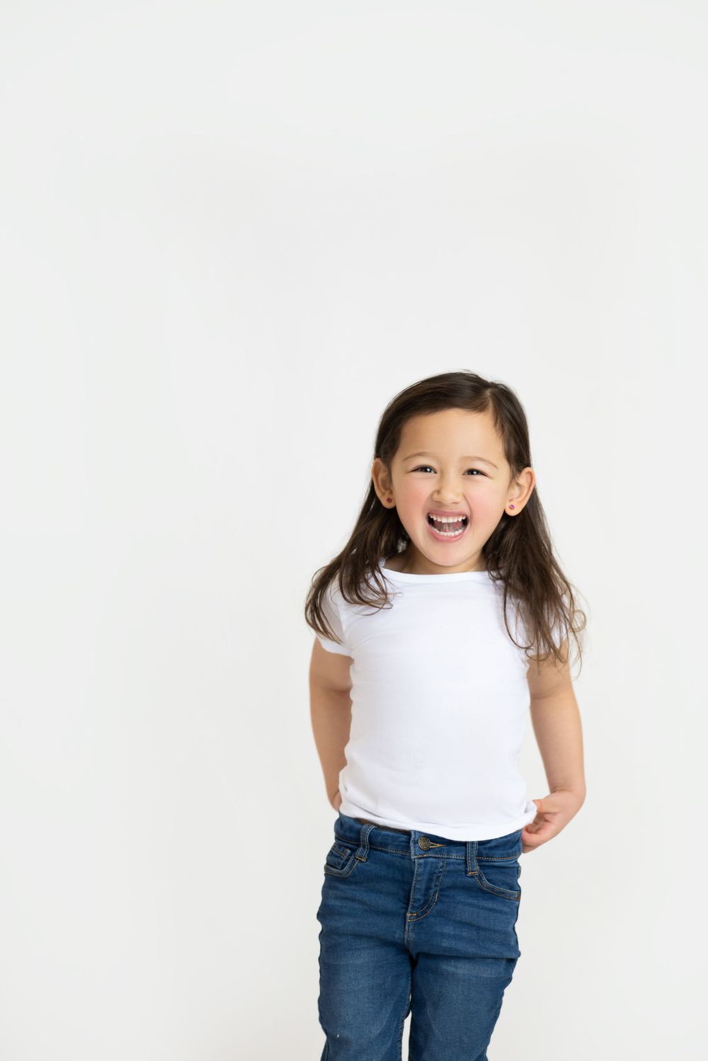 A young child wearing a white t-shirt and blue jeans laughs joyfully against a white background.