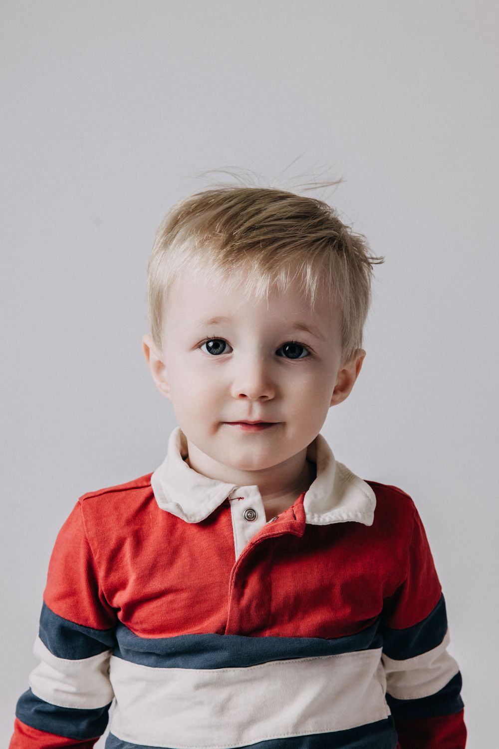 Child wearing red and white striped polo shirt poses against grey background.