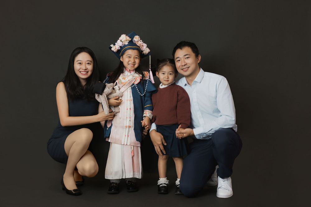 Family of four posing for a portrait, with a girl in traditional dress and floral headpiece, against a dark background.