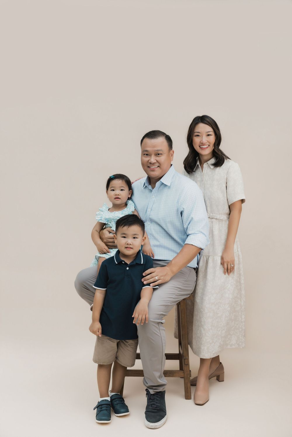 Asian family of four posing for a studio portrait, parents with two young children against a beige background.