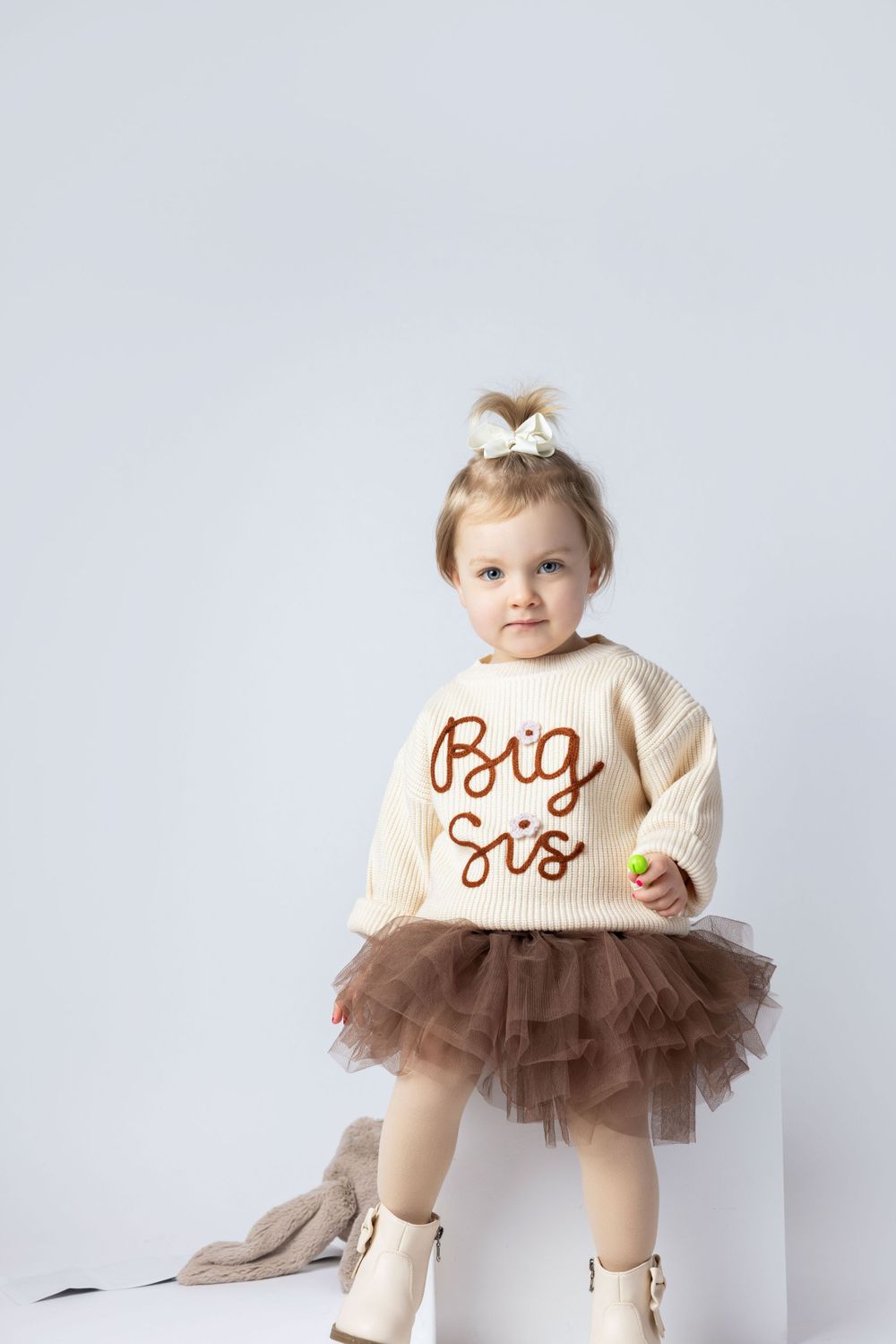 Toddler wearing tulle skirt and cream sweater with 'Big Sis' text poses against white background.