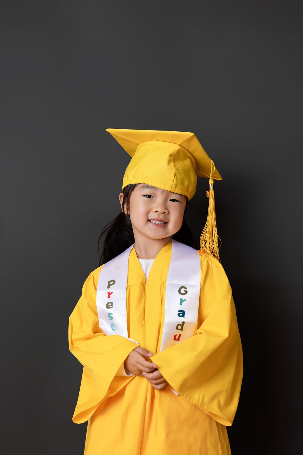 A graduate wearing a bright yellow cap and gown poses against a dark background for a series of four photos.