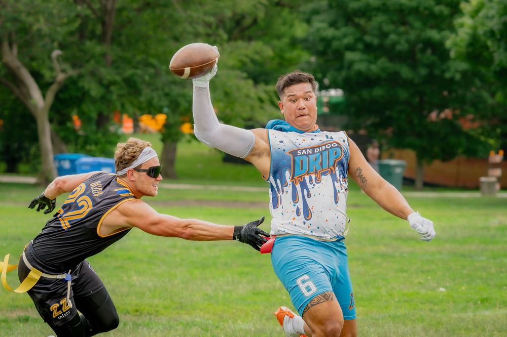 An athlete from San Diego Drip extends his arm overhead with the football while another athlete pulls his flags to stop the play