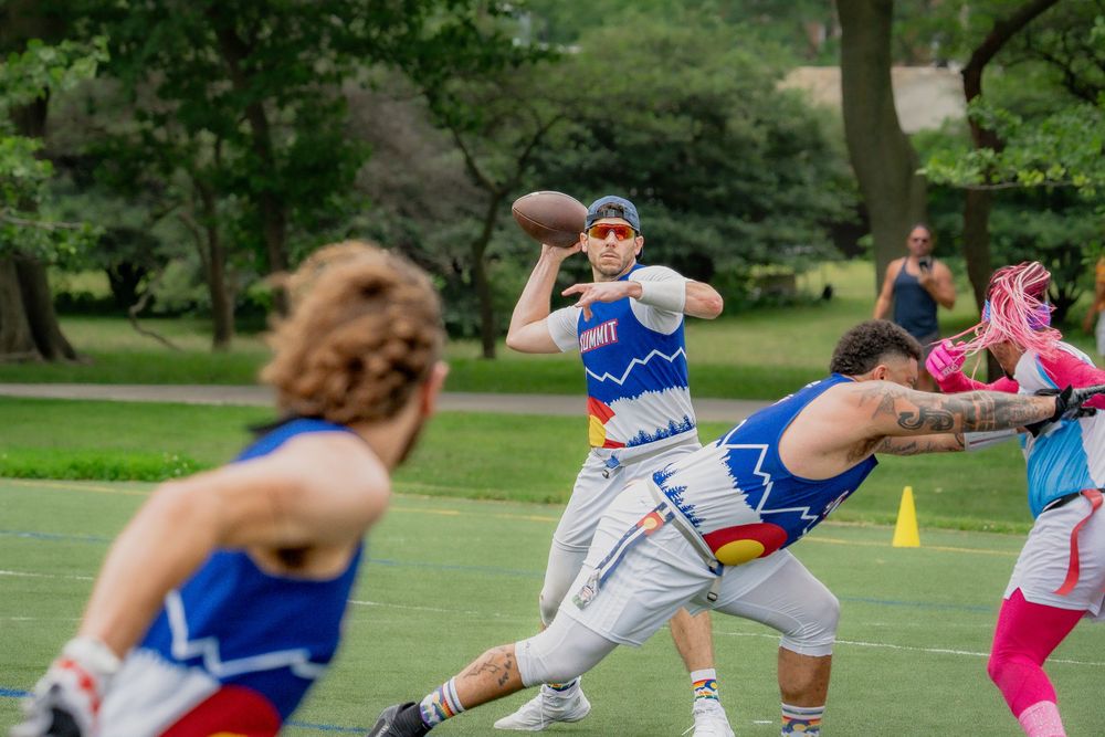 The quarterback from the Denver Summit begins to throw a pass to an athlete while a blocker pushes the defense's rusher out of the way