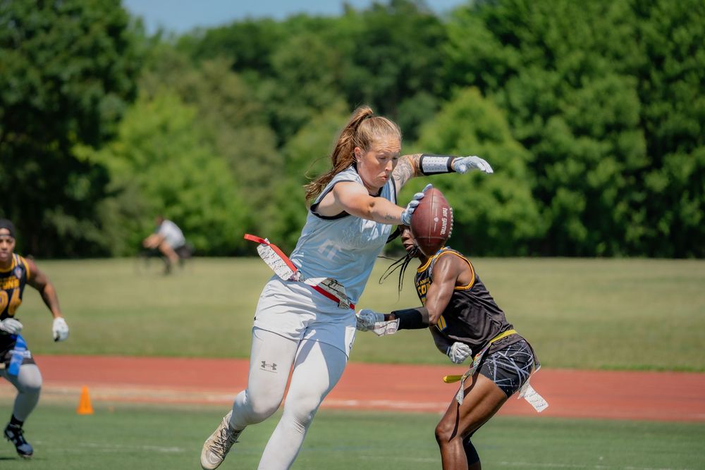 An athlete extends her hand with the football to gain yards while another pulls her flags to stop the play at Pride Bowl