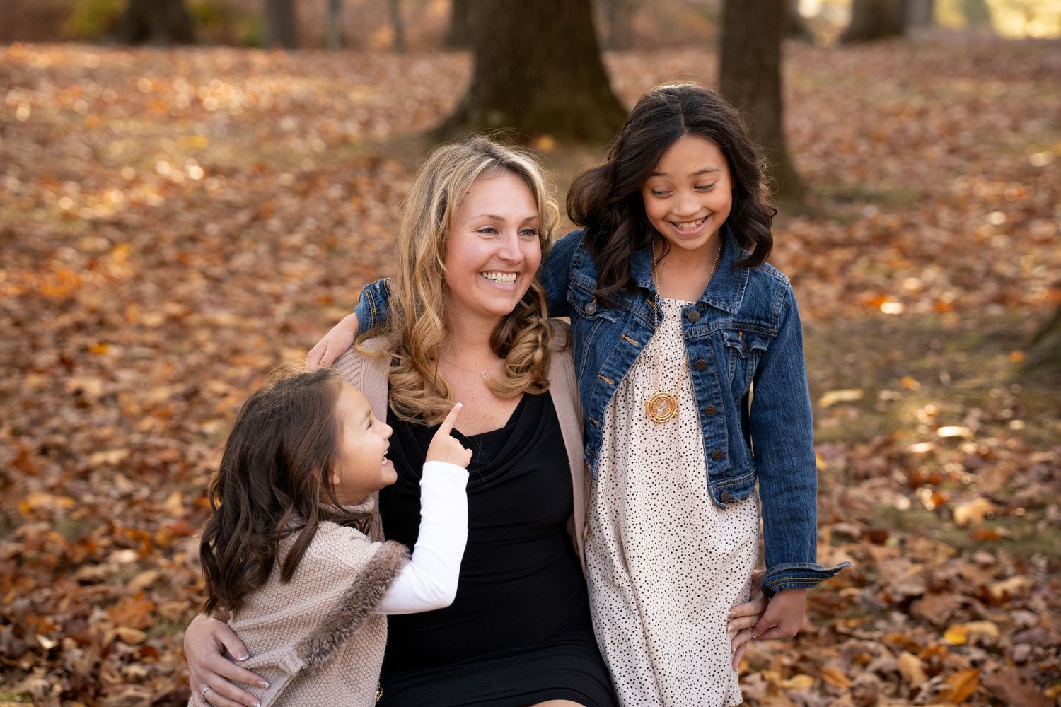 Group of people laughing together while sitting on fallen autumn leaves at outdoor photoshoot. Children being silly.