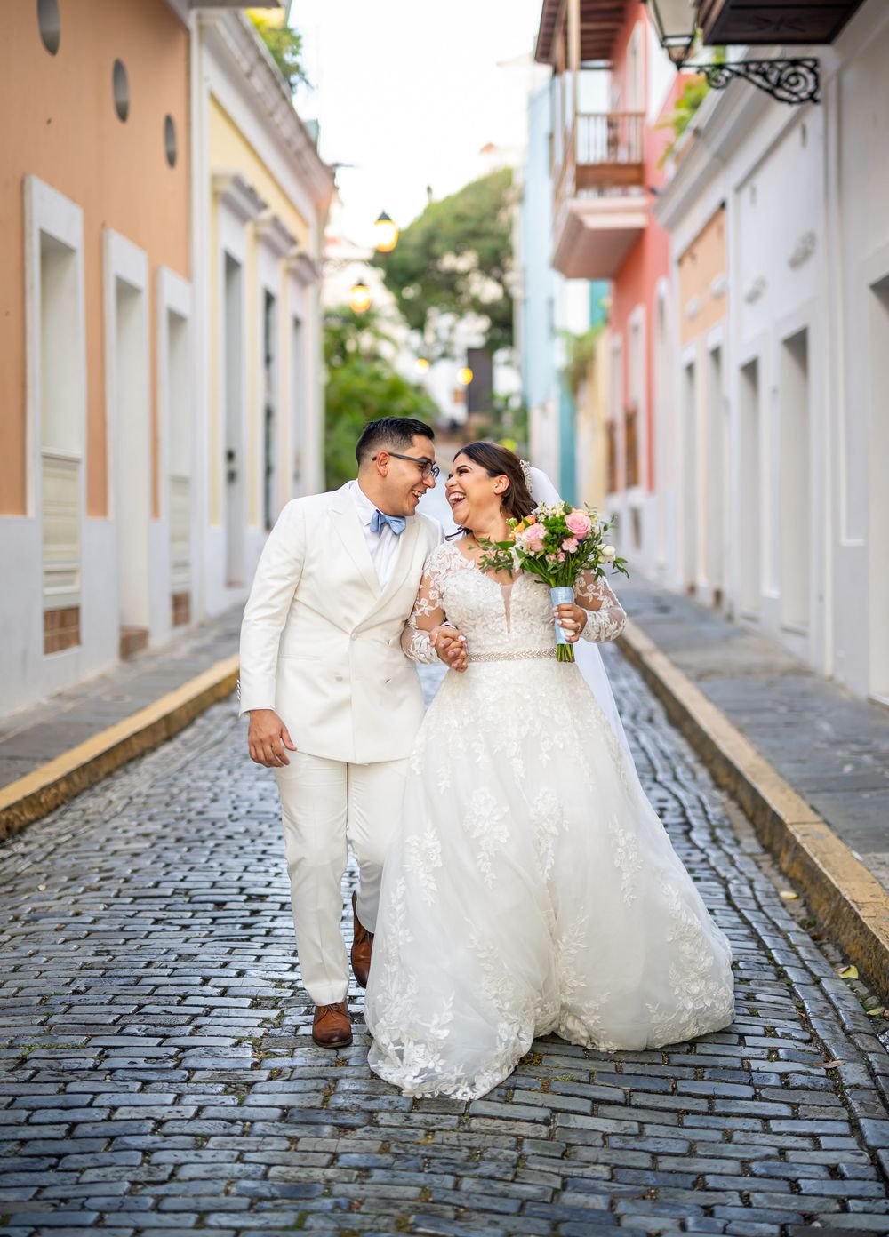 Newlyweds walk hand in hand on a charming cobblestone street in Old San Juan with historic pastel buildings.