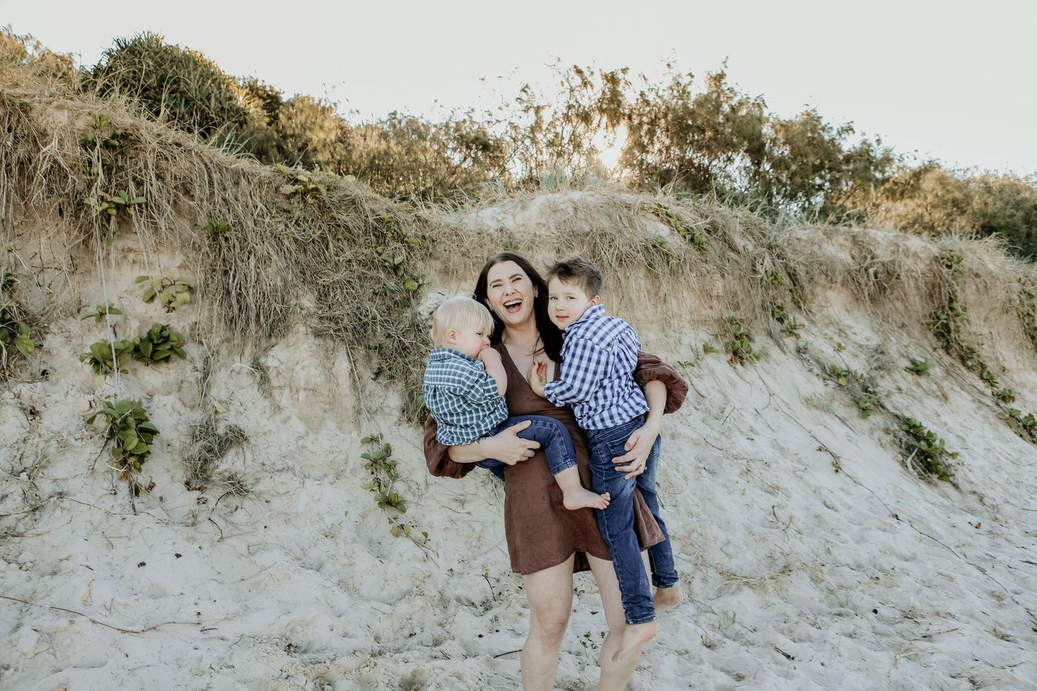 Family enjoying a playful moment together on sandy hillside dunes at sunset.