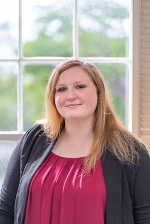 A professional portrait of someone in business attire by a bright window.