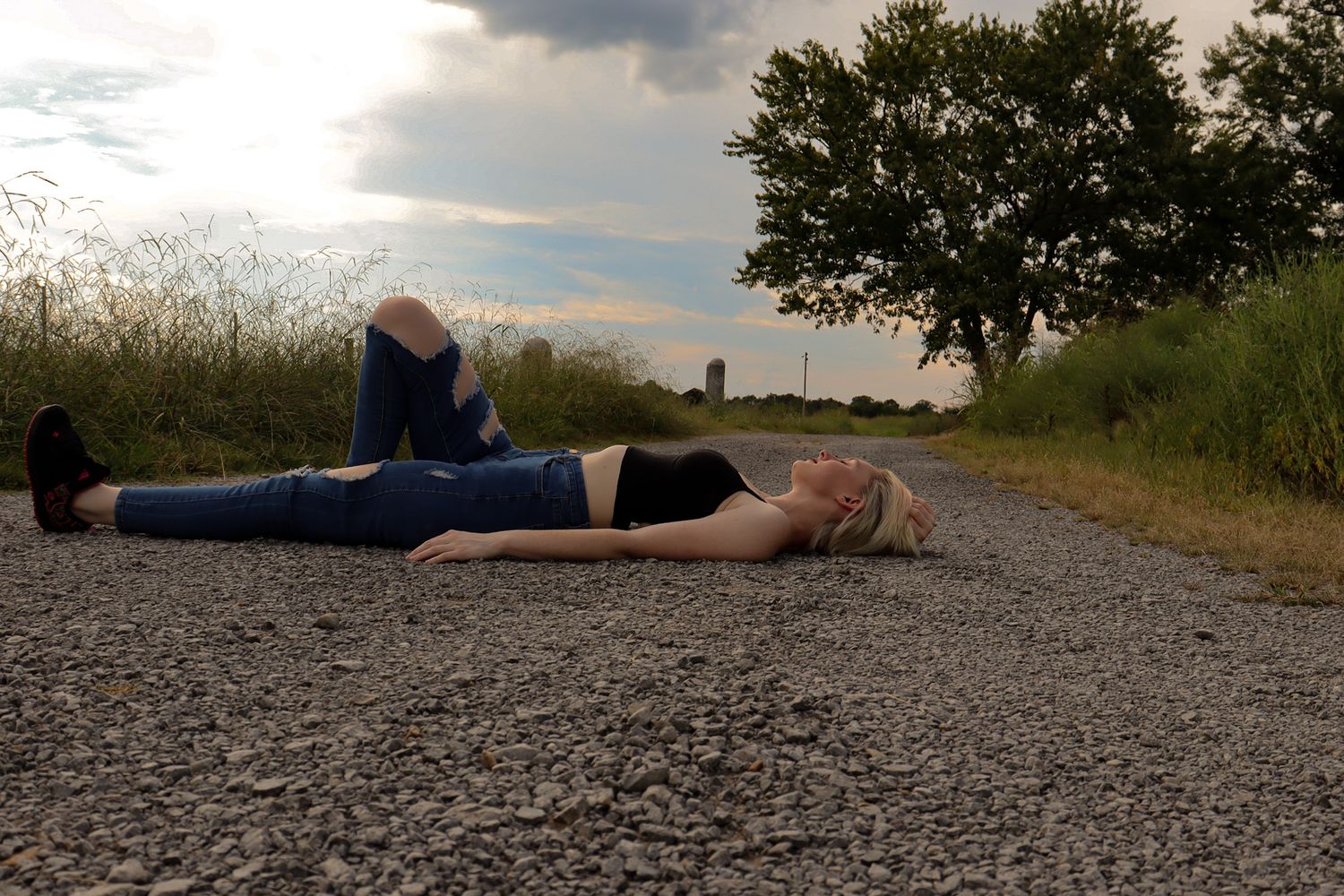 Row of figures laying on a gravel path during sunset with natural scenery in background.