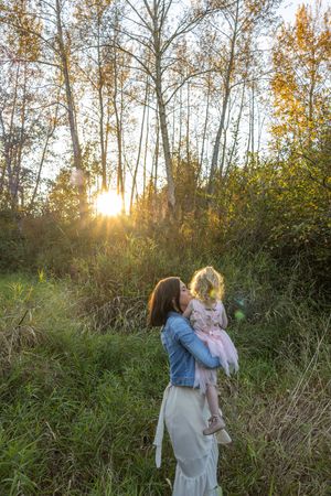Mom and daughter dancing in tall grass in front of trees during golden hour.