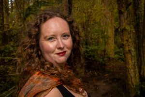 Woman portrait in the forest with blonde curly hair and wearing orange scarf.