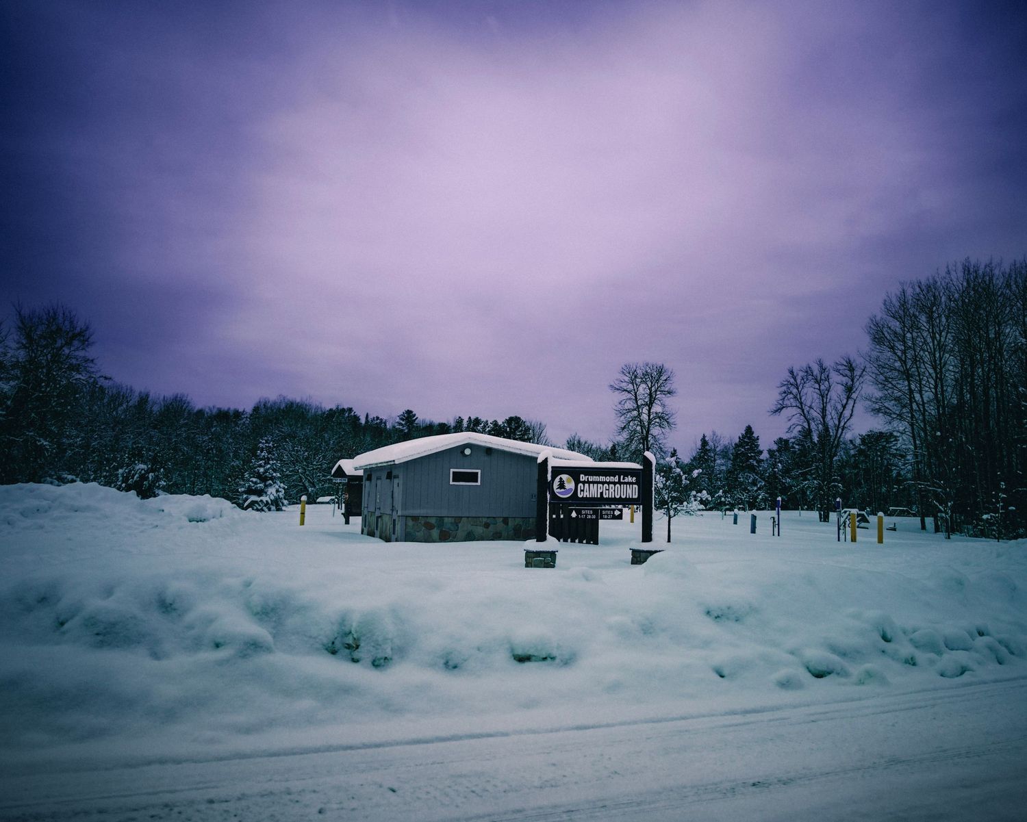 Snowy winter landscape with ski slopes and buildings in the distance under a moody purple sky.
