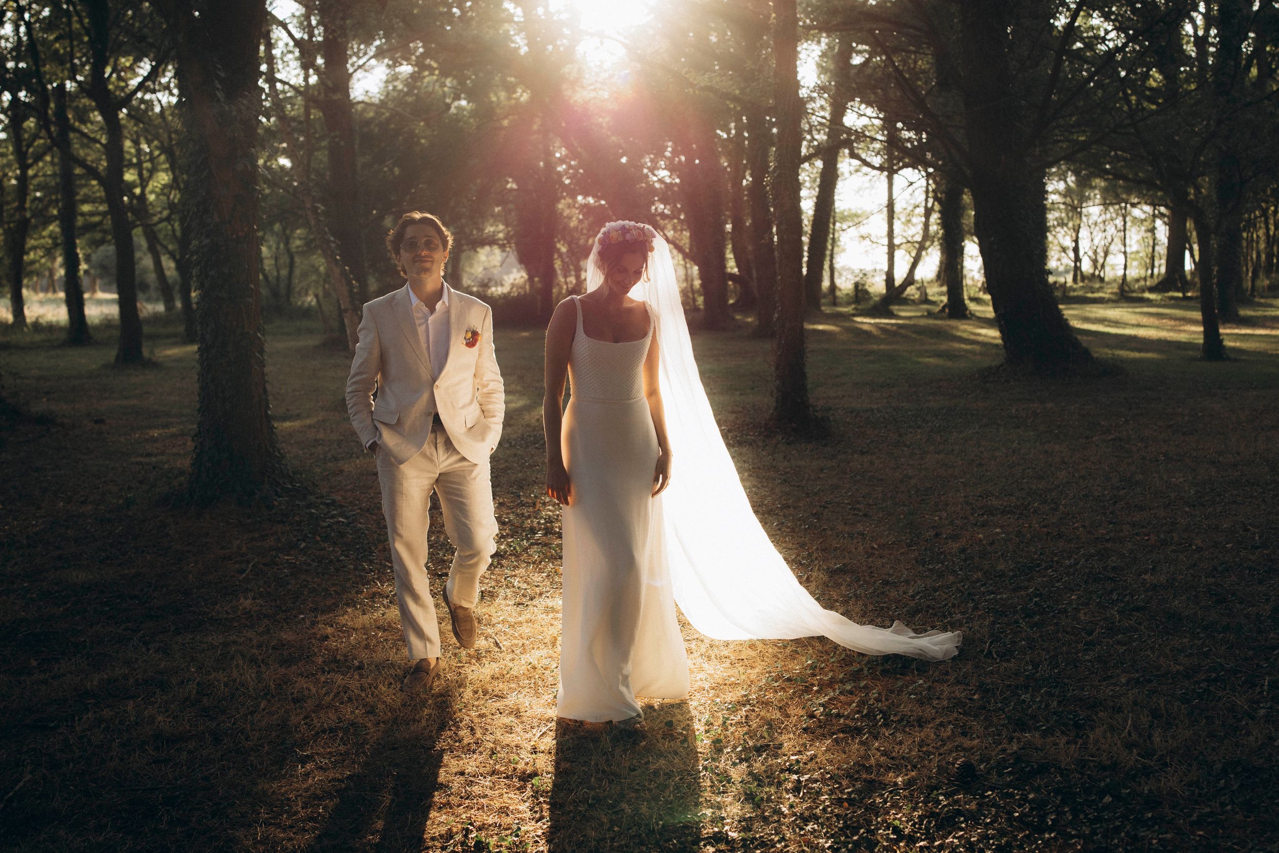 Silhouetted couple stands in sunlit forest with golden light streaming through trees during sunset photo session.