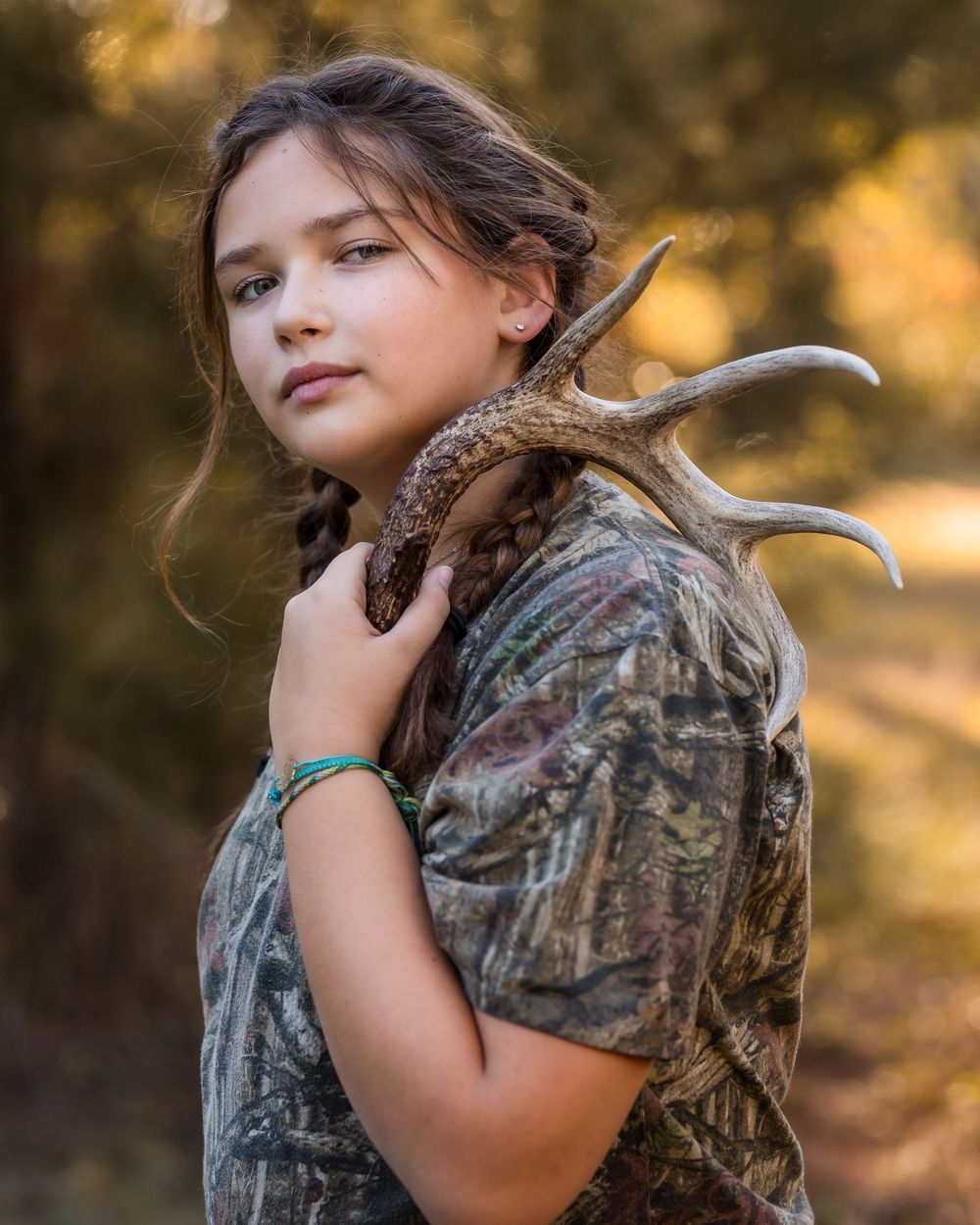 Young hunter in camouflage clothing poses with a deer antler during a successful hunting trip photo shoot.