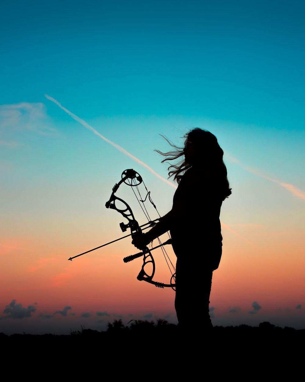 Silhouetted archer in a dramatic sunset drawing bow against vibrant turquoise and orange sky.