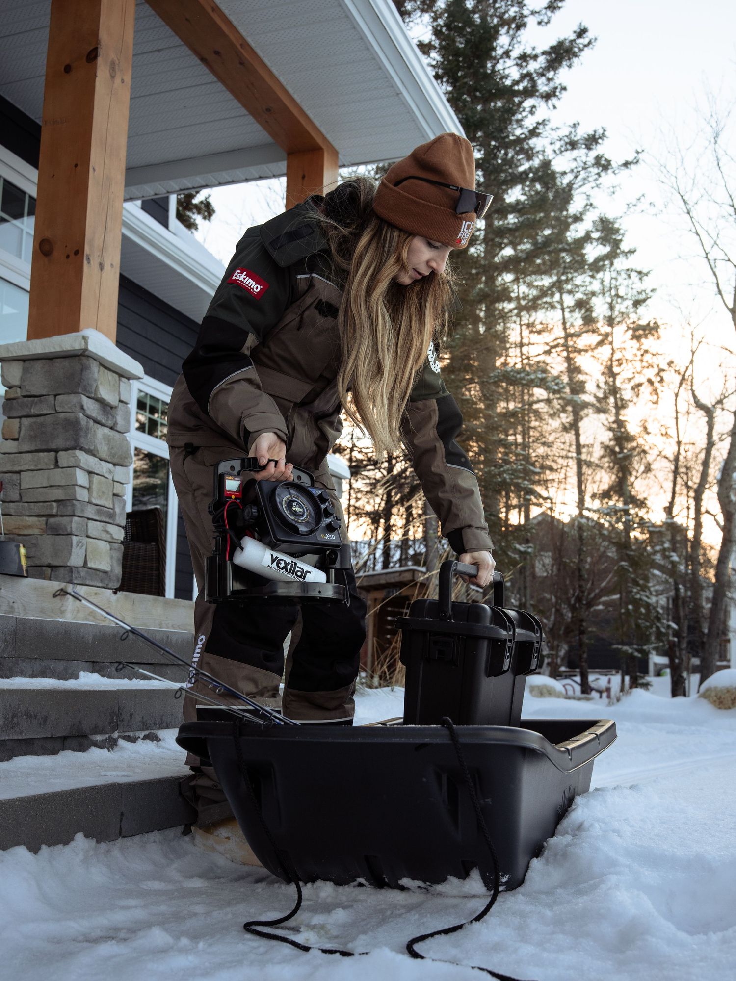 Person setting up ice fishing equipment on snowy porch steps with storage containers.