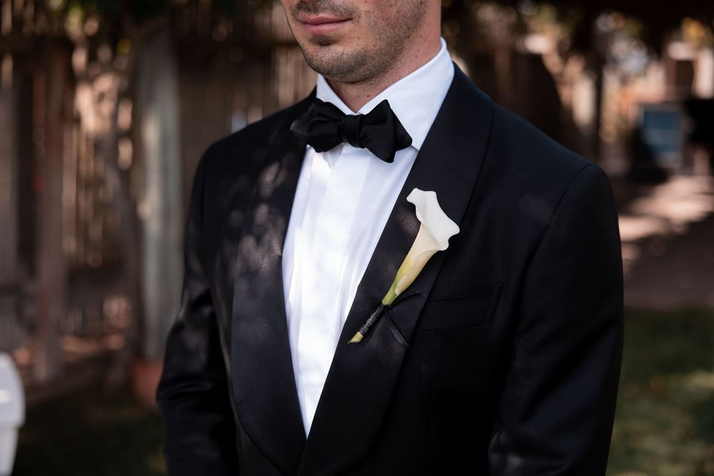 A group of groomsmen in black tuxedos and bow ties stand together at a formal wedding event.