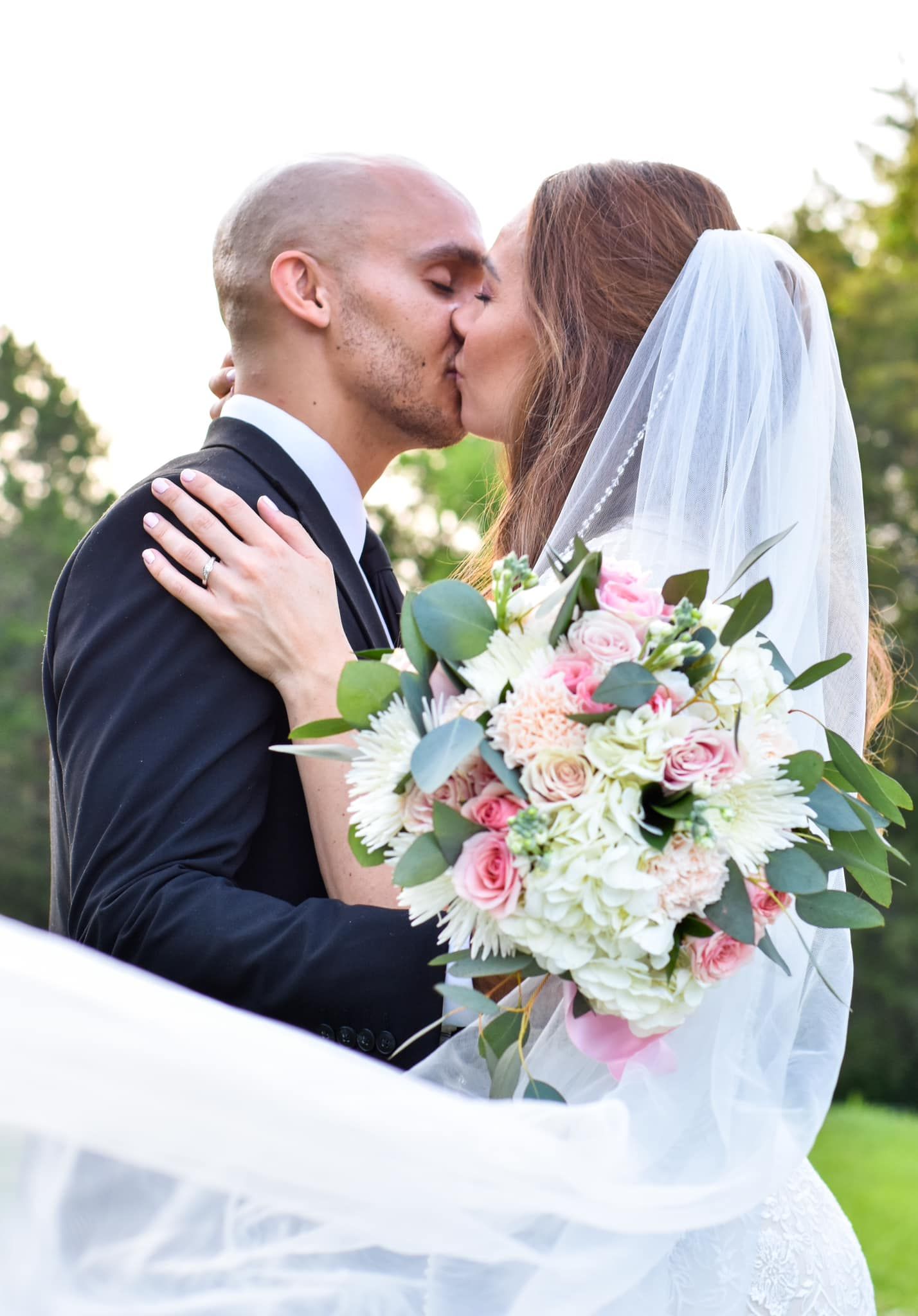 A bride and groom share intimate moments in an outdoor garden setting with a beautiful floral bouquet.