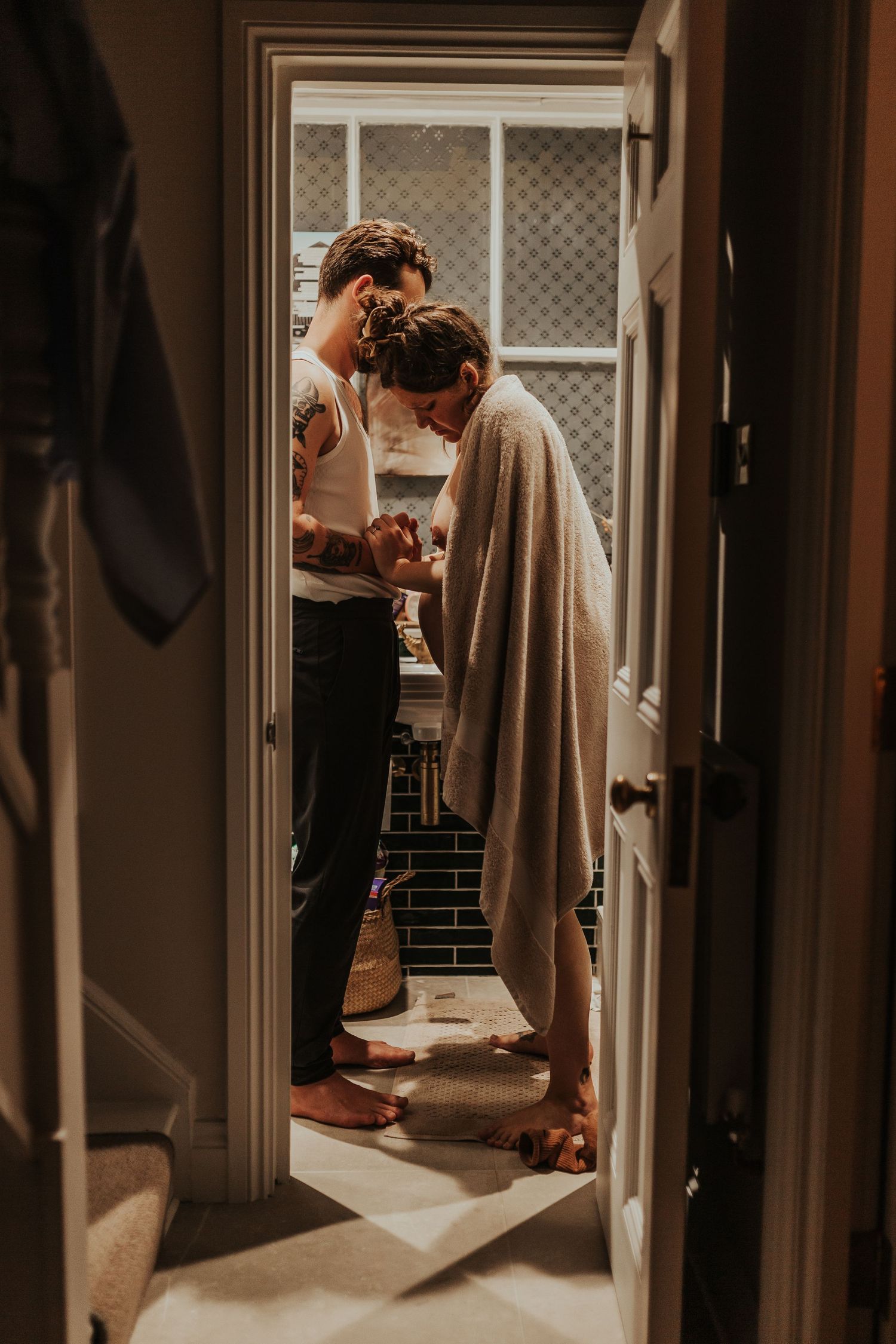 A couple shares an intimate moment in a sunlit doorway during their wedding day preparations.