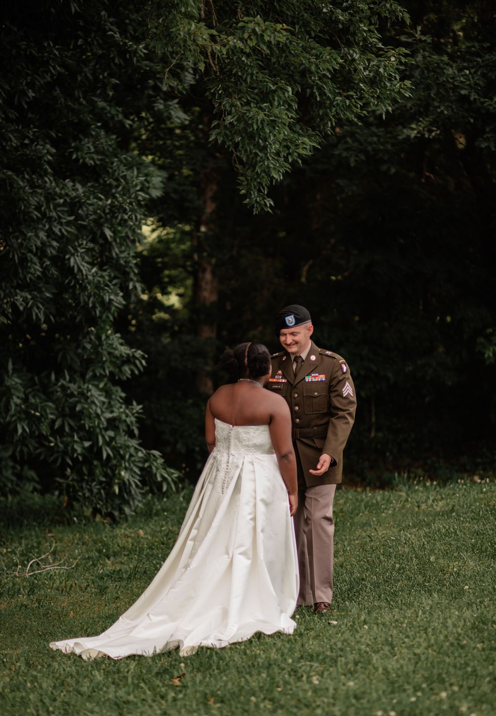 A couple shares an intimate moment on a grassy slope during their wedding photoshoot.