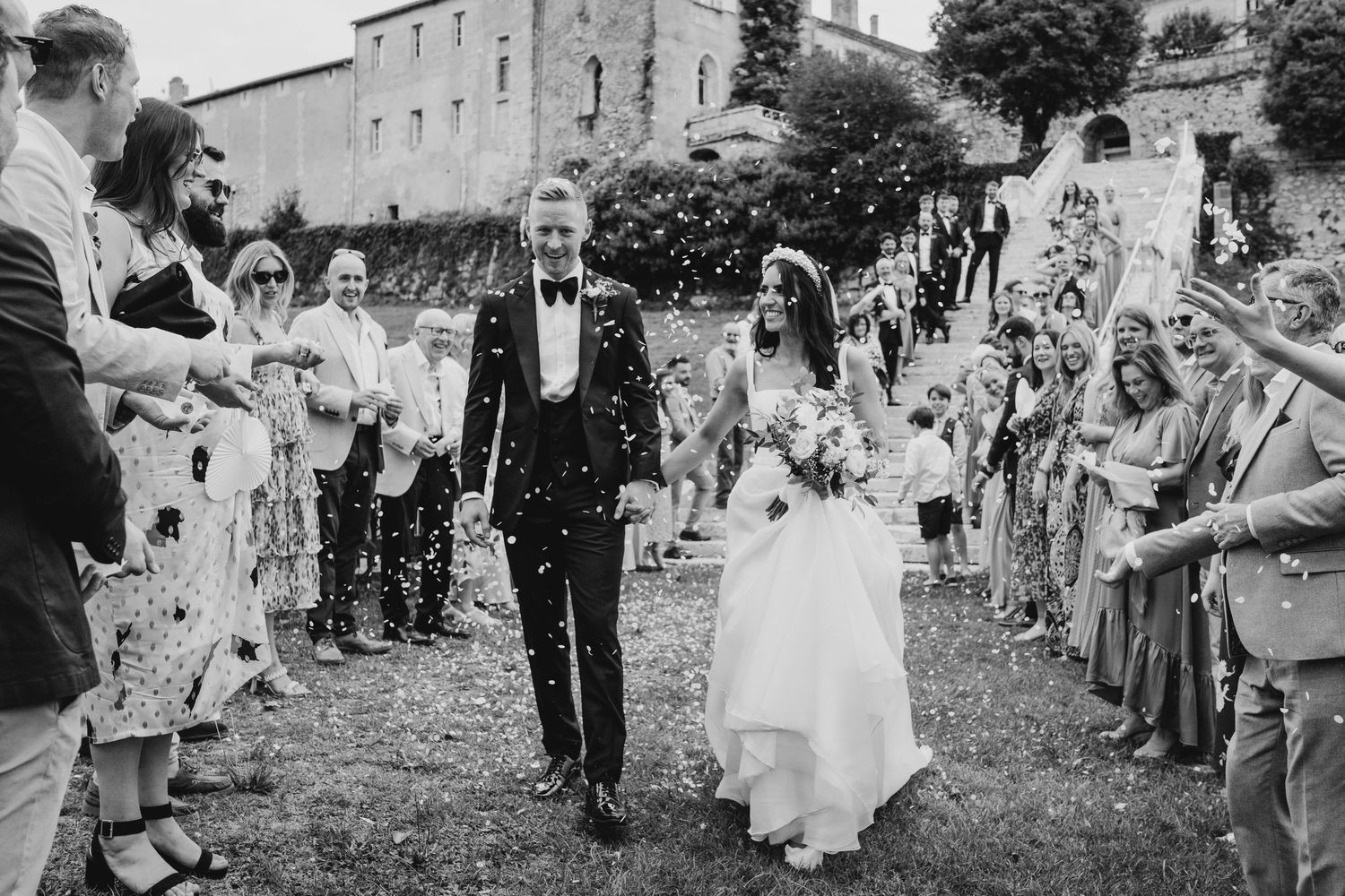 Wedding guests line a pathway throwing confetti as newlyweds walk through during an outdoor celebration at a rustic venue.