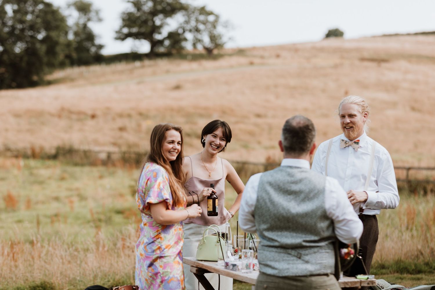 A group enjoying drinks reception on a grassy hillside with wine glasses and conversation on a sunny afternoon.