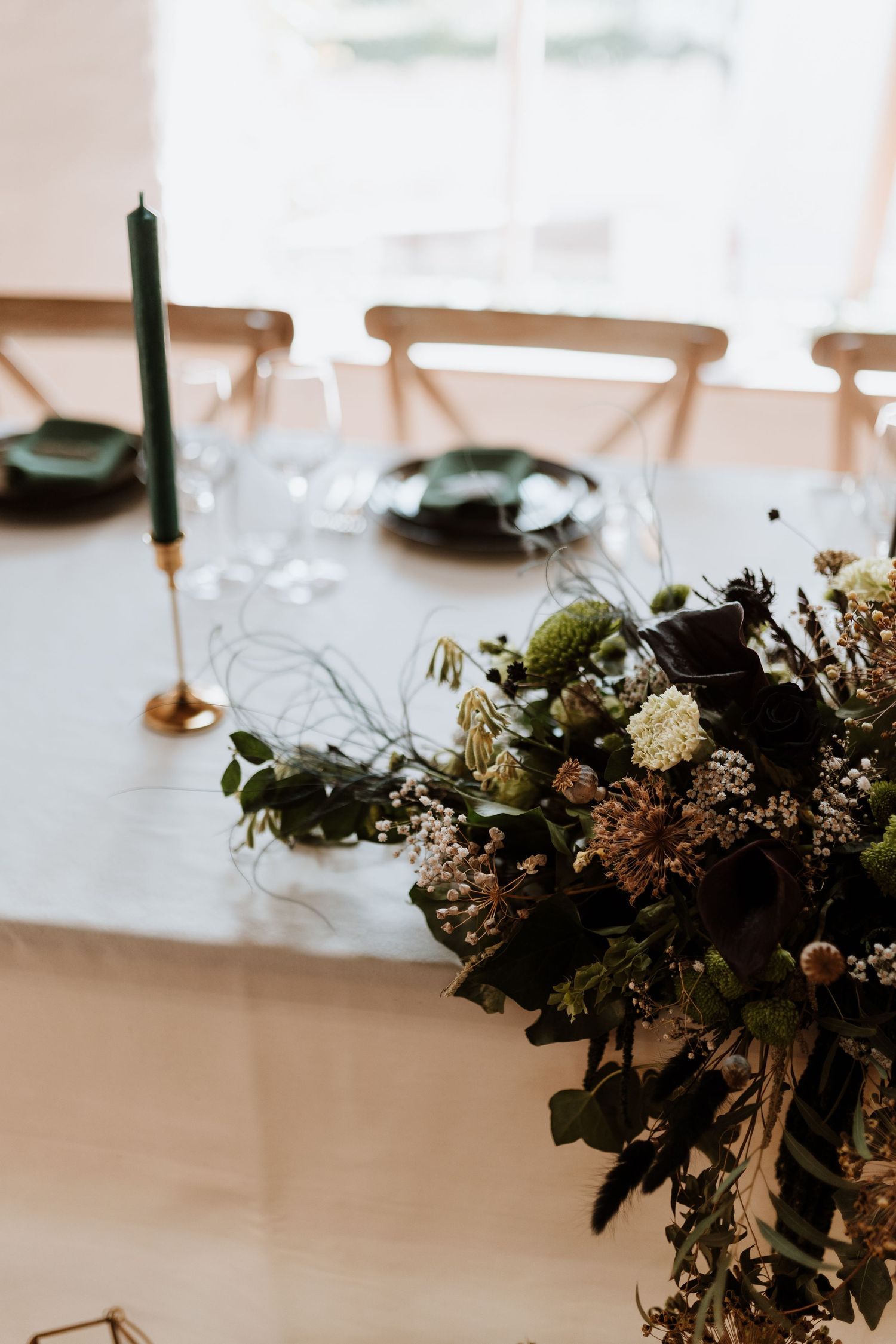 Elegant floral table centerpiece with greenery and white flowers on a white tablecloth with candlesticks in soft lighting.