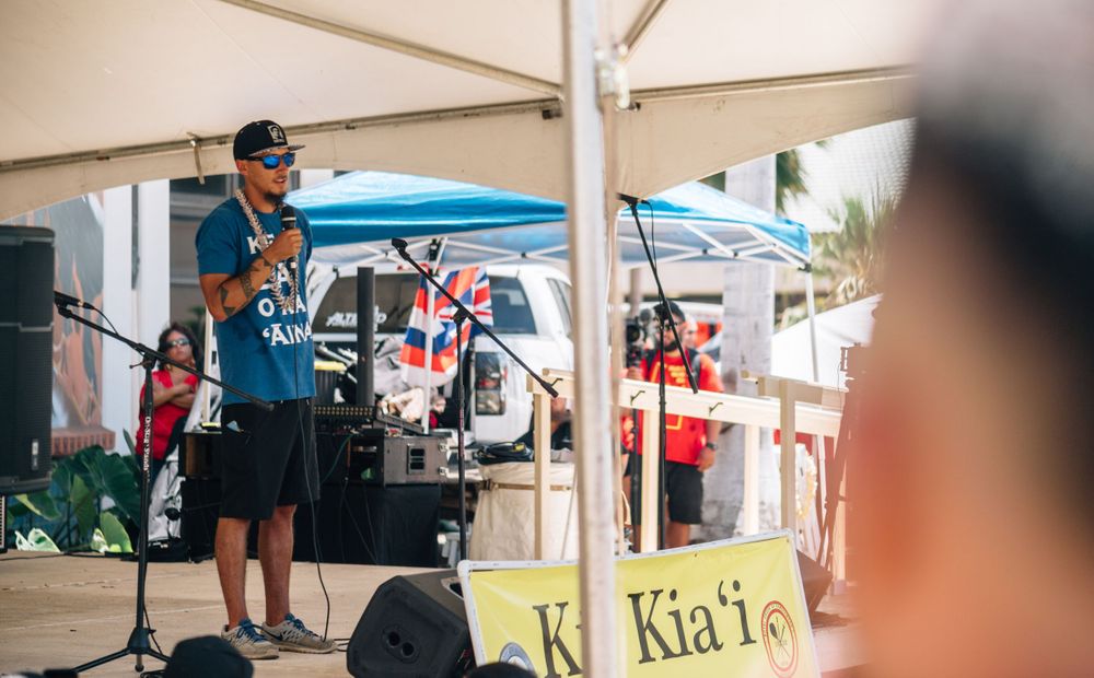 A performer in a blue shirt entertains a crowd under a white canopy tent.