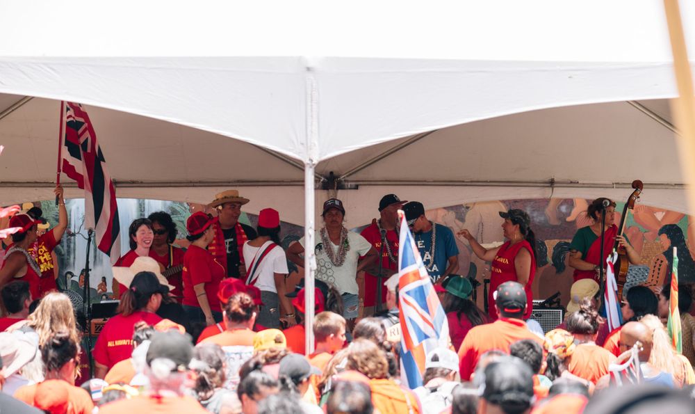 A crowded outdoor event tent filled with people wearing red clothing and waving flags.