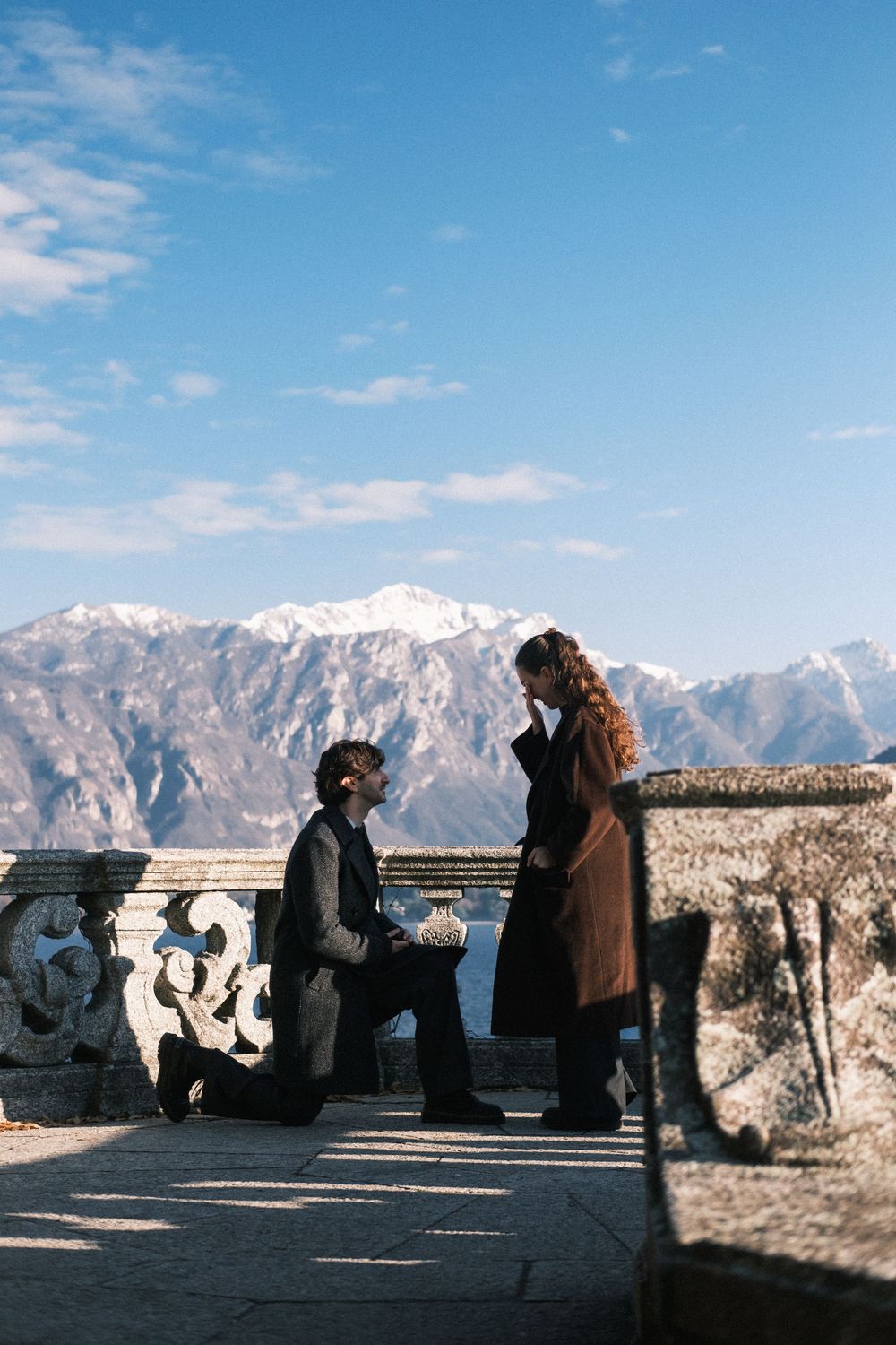 People silhouetted against snowy mountain peaks at a scenic overlook on a bright sunny day.