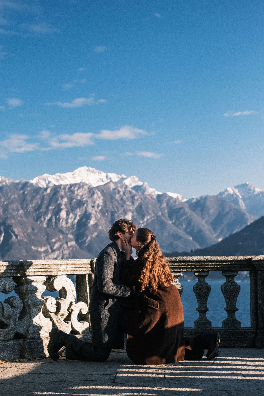 A panoramic sequence of people enjoying views of snow-capped mountains from a stone balcony on a clear sunny day.