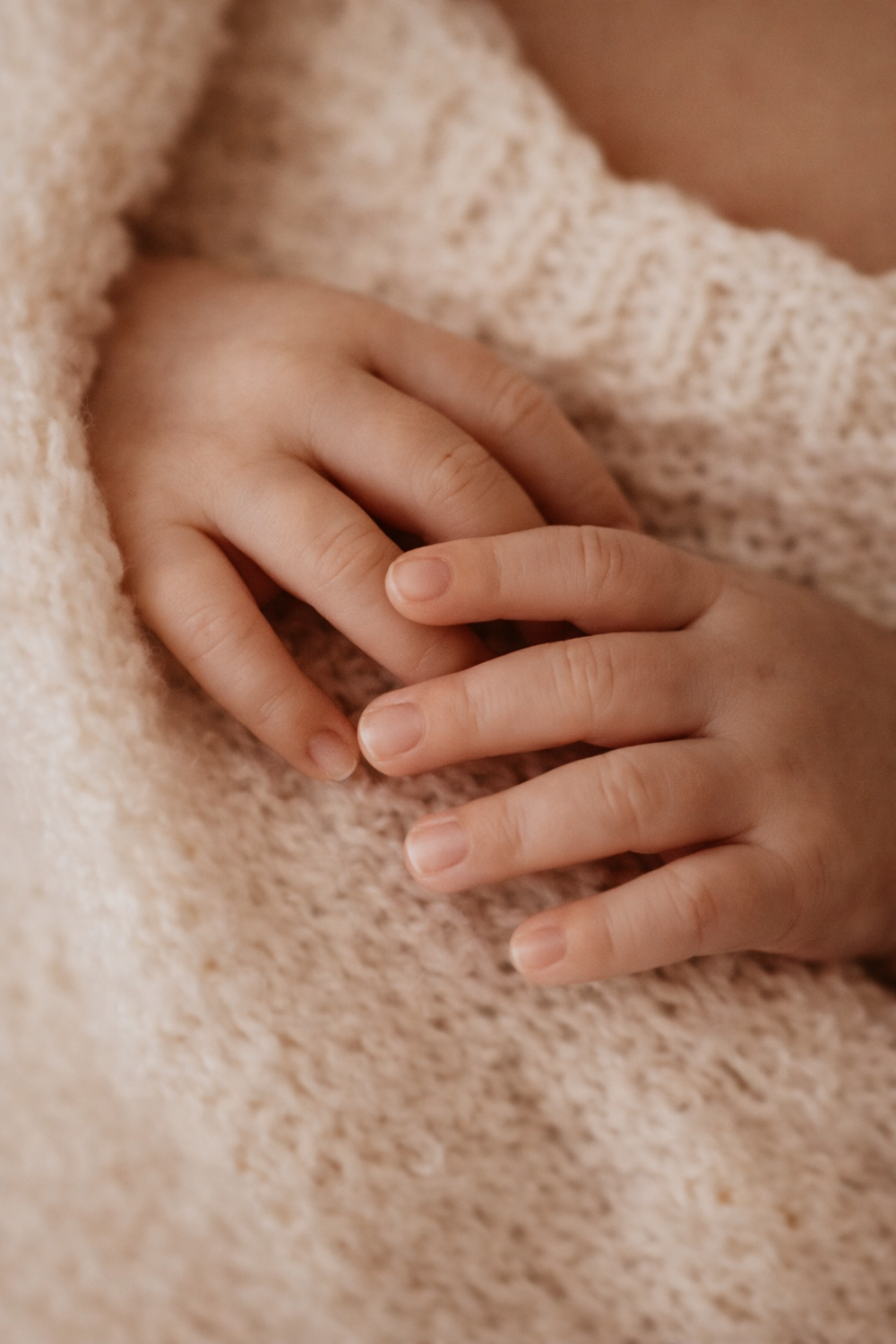 Close-up of small hands gently resting on soft knitted beige fabric.