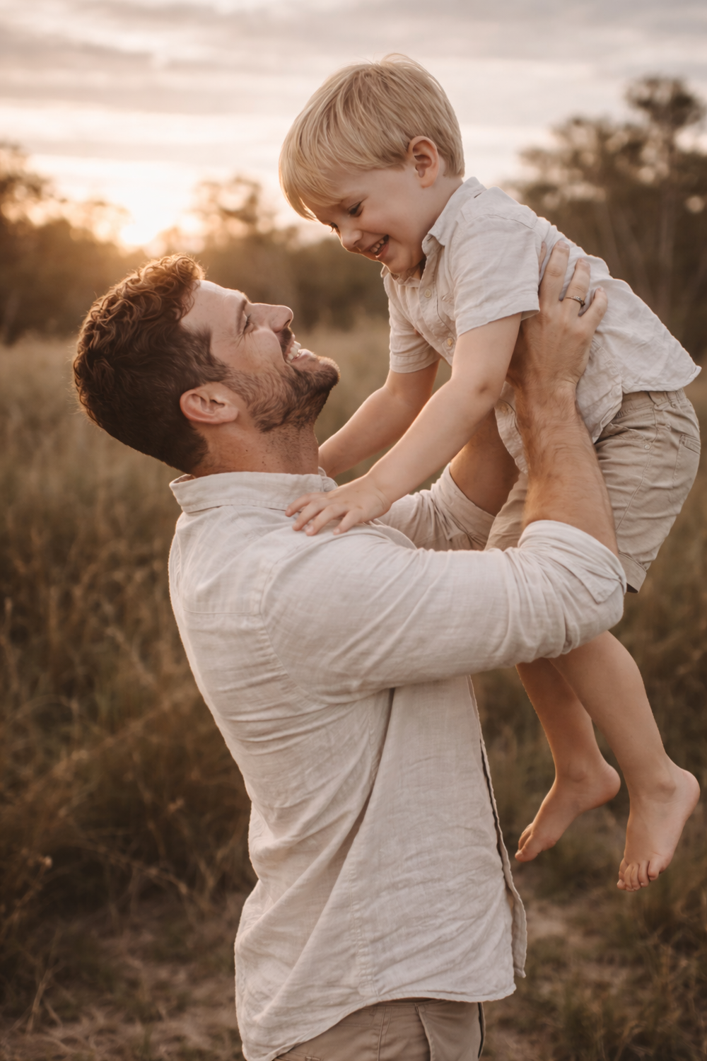 Joyful playtime moment captured at sunset with lifted child against golden sky.
