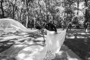 Black and white photo of a bride and groom in a park, with her veil billowing in the wind.
