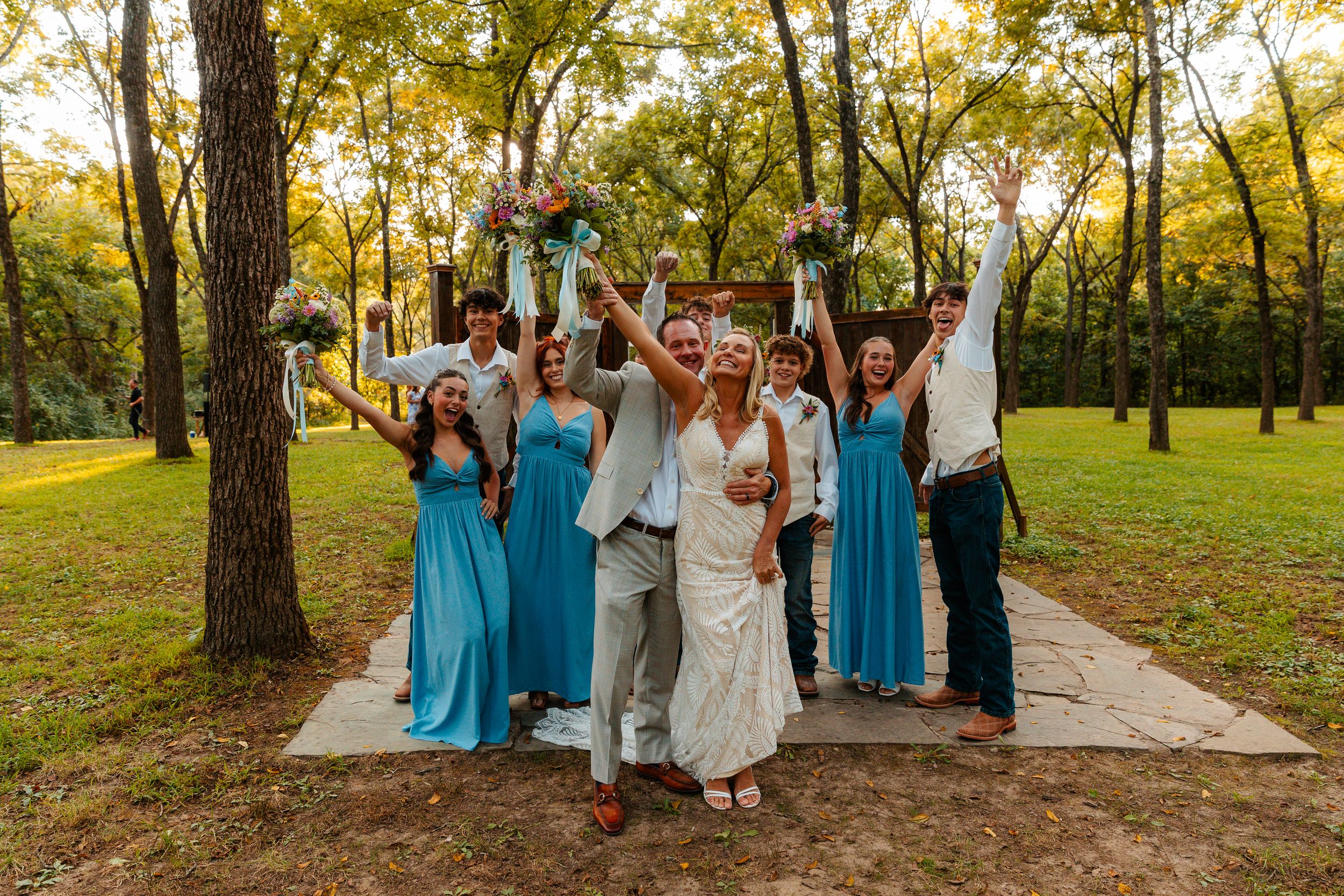 Wedding party celebrating on a tree-lined path with bridesmaids in blue dresses. wedding photography st louis