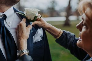 Close-up shot of someone adjusting a white rose boutonniere on a formal suit jacket. wedding photography st louis