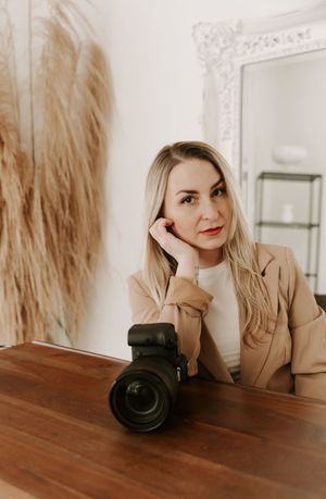 Photographer with camera on wooden desk in bright studio with ornate white mirror and pampas grass decor.
