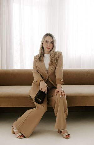 Professional portrait in tan blazer suit sitting on brown couch in bright minimal studio setting.