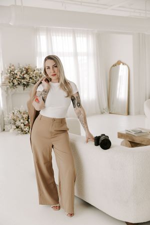 Fashion blogger styling beige wide-leg trousers with white top in minimalist bedroom setting.