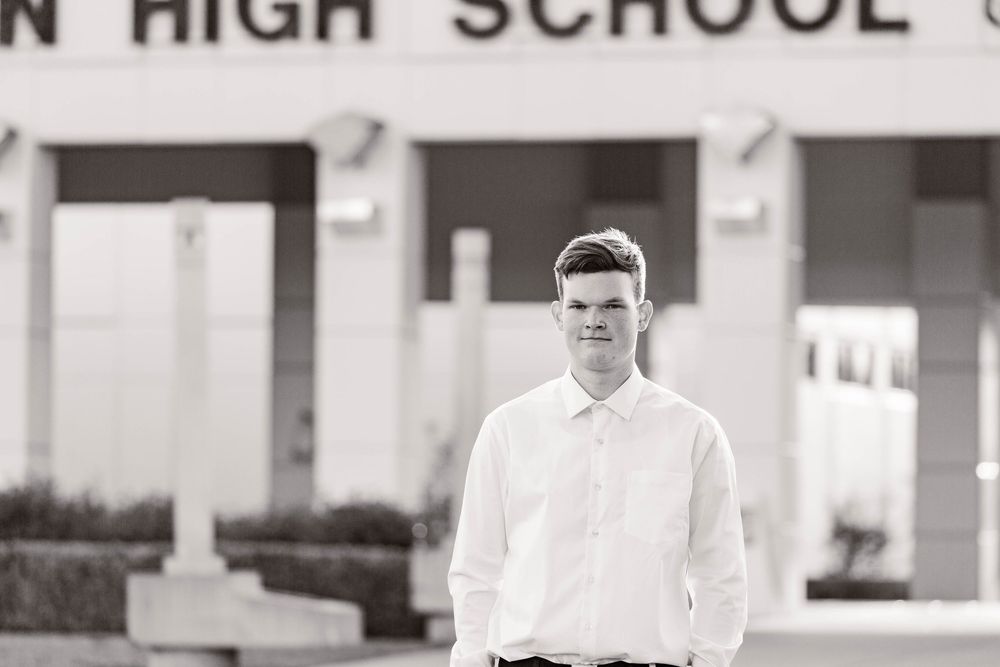 Black and white portrait of a student in a white shirt standing outside a high school building.