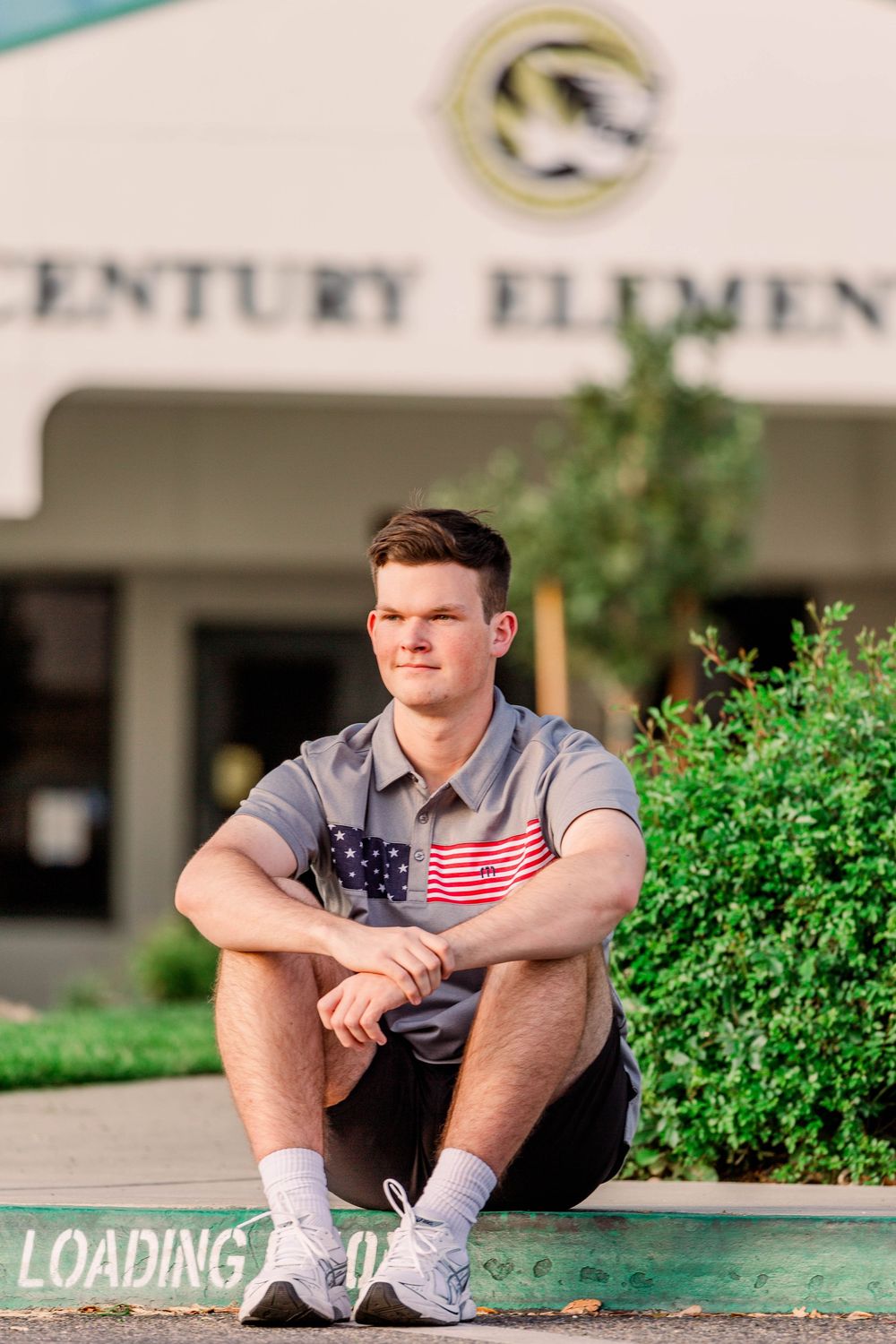 Person sits casually on steps outside Century Elementary wearing shorts and a gray shirt.