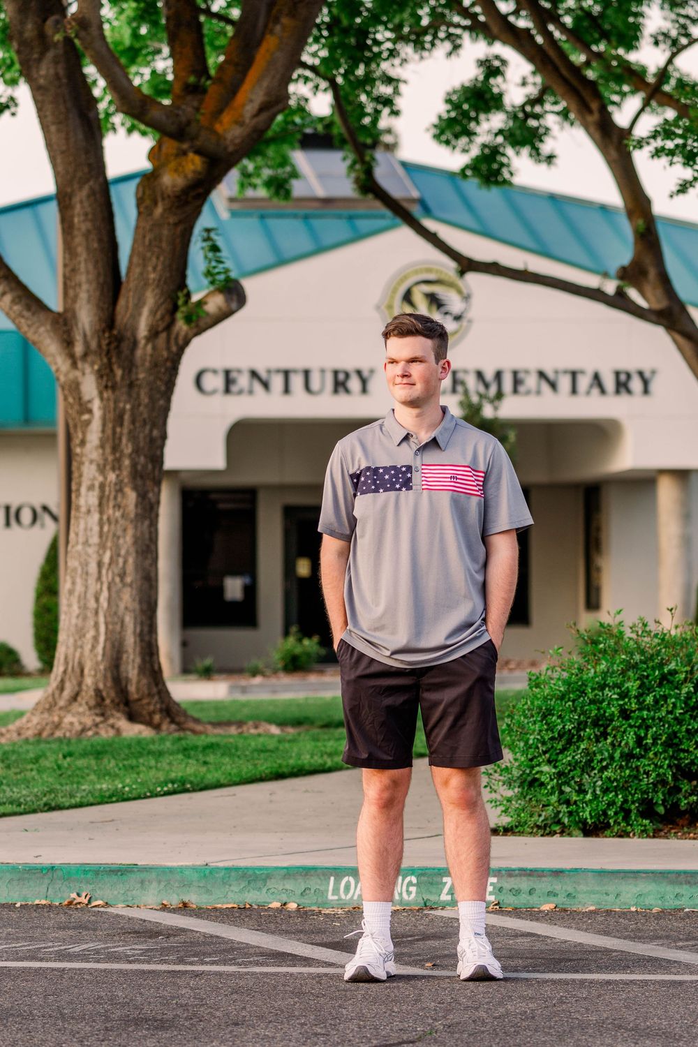 Student stands in front of Century Elementary school entrance wearing a gray t-shirt and dark shorts.
