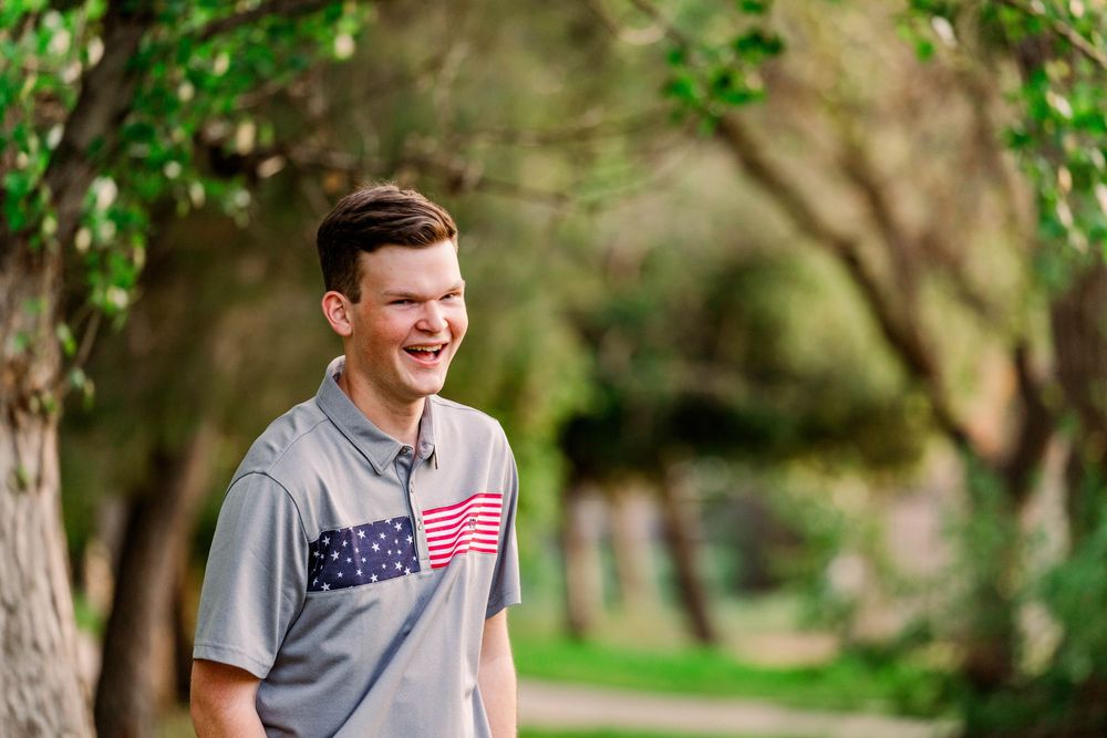 A person in patriotic attire smiles while standing in a lush green outdoor setting.