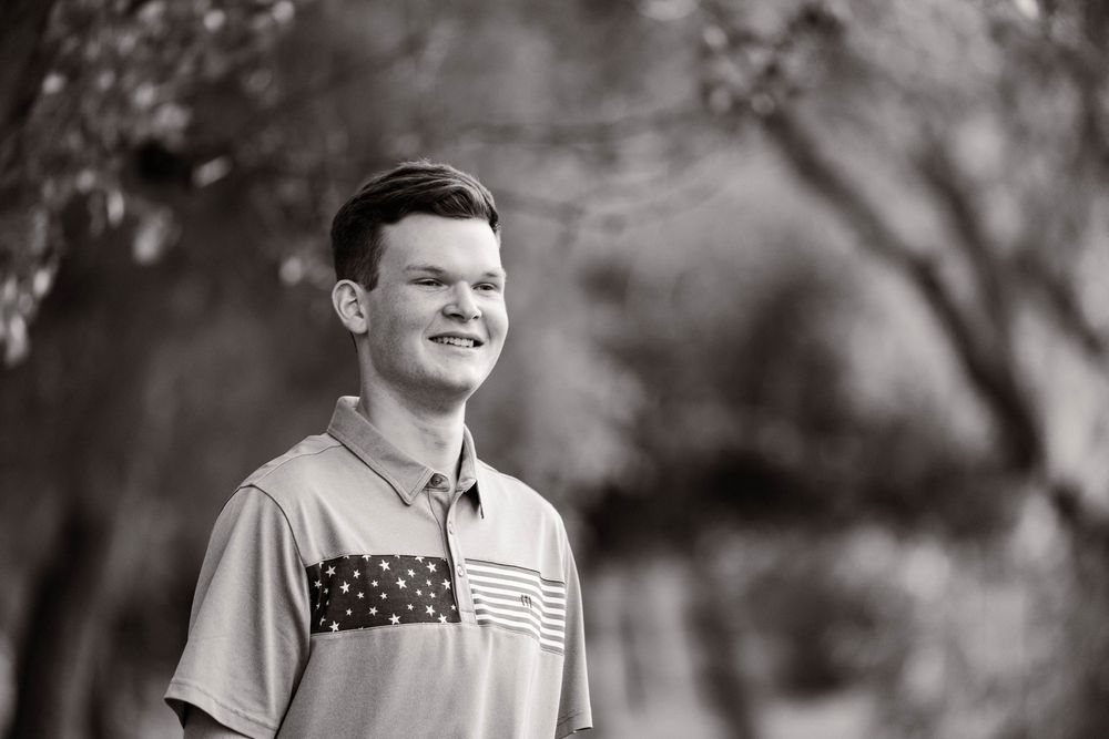 Black and white portrait of a student smiling outdoors with trees in background.
