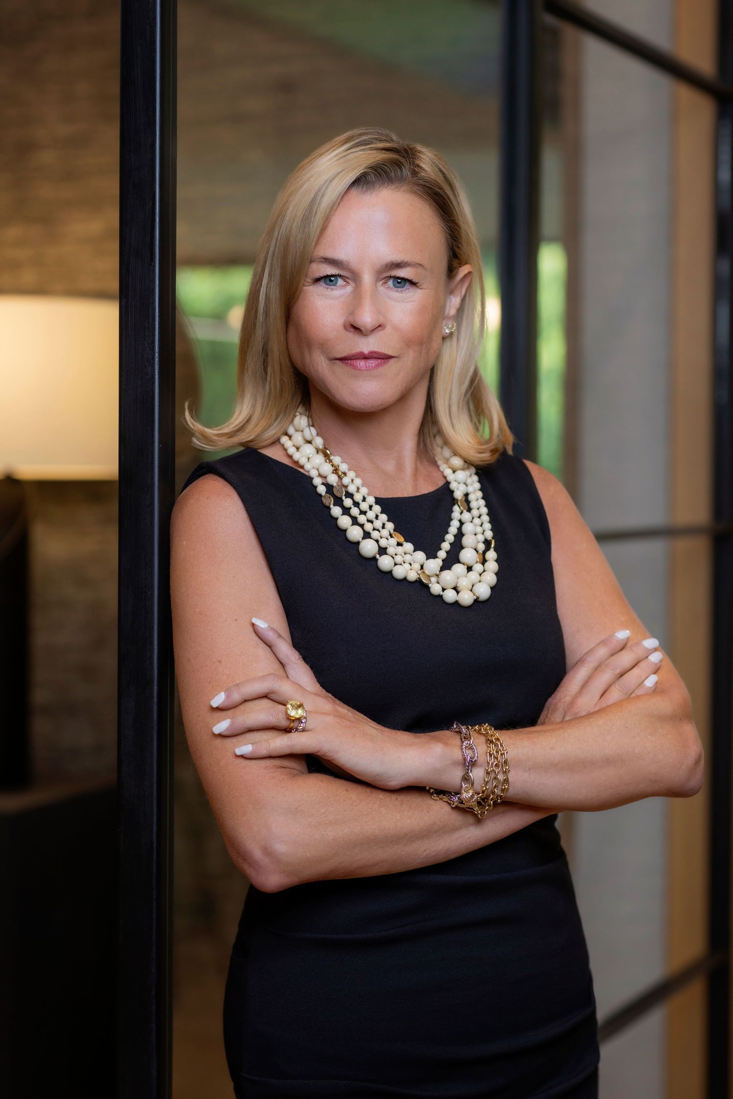 Professional portrait of someone in a black sleeveless dress with layered pearl necklace and arms crossed.
