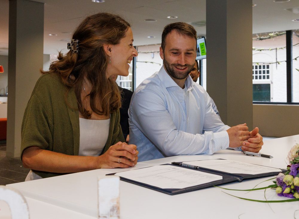 Bruidspaar lacht bij het ondertekenen van de trouwakte op het gemeentehuis - documentaire trouwfotografie - gemeentehuis Boxtel - MaxFotos