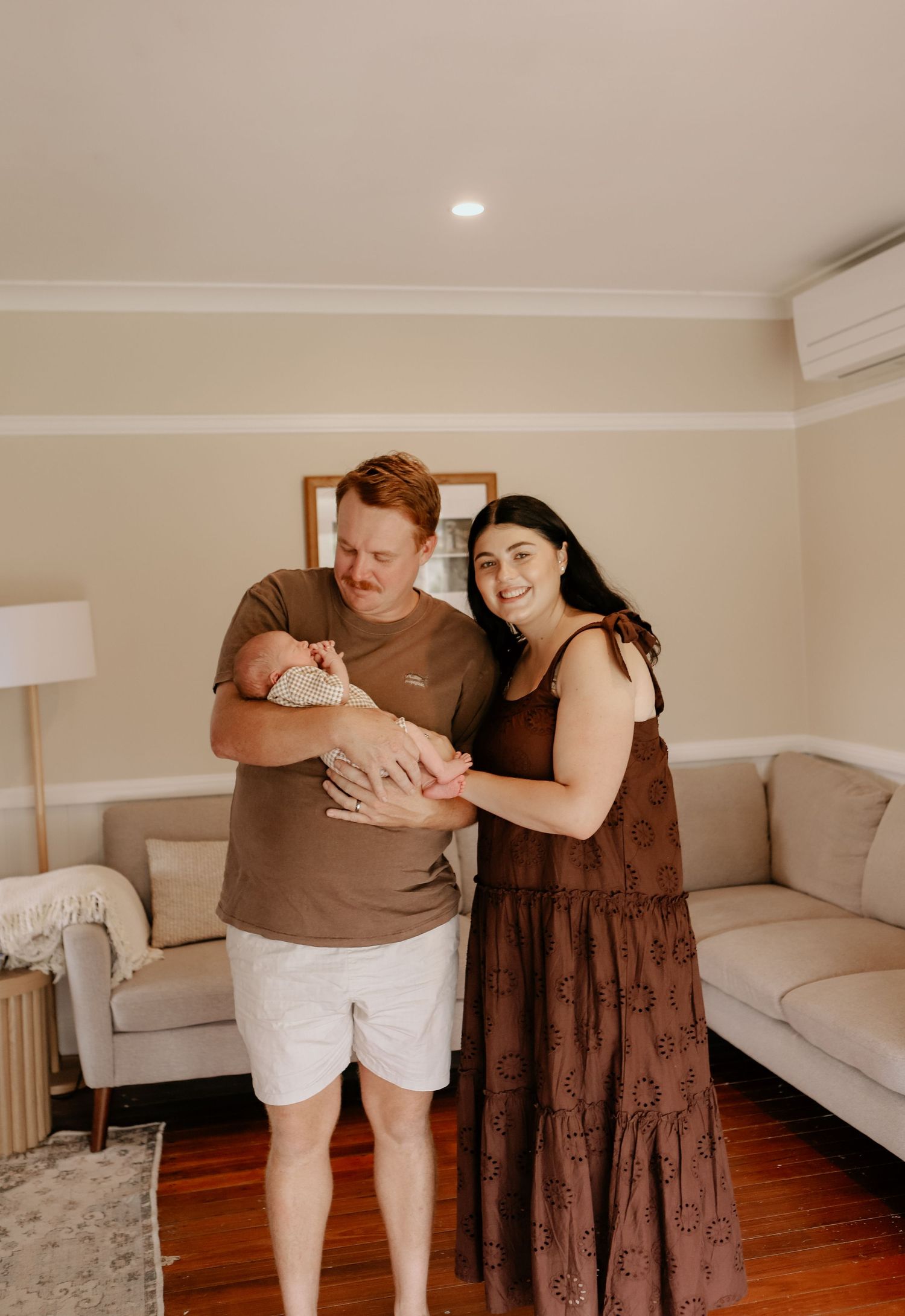 A series of intimate family moments captured in warm tones showing parents with a newborn baby in a cozy living room setting.