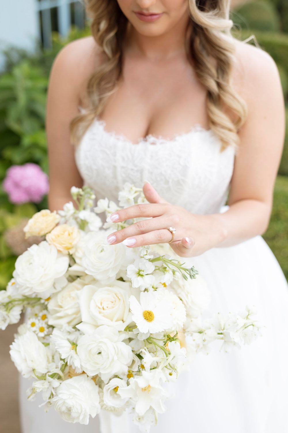 Close-up of bride's white rose and daisy wedding bouquet against lace dress.