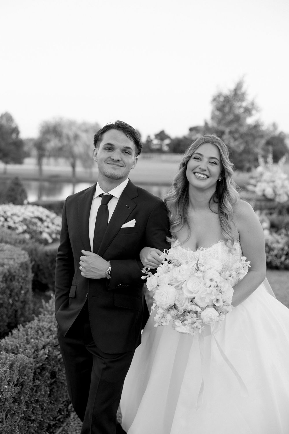A romantic wedding portrait of a couple outdoors with the bride holding a white floral bouquet.